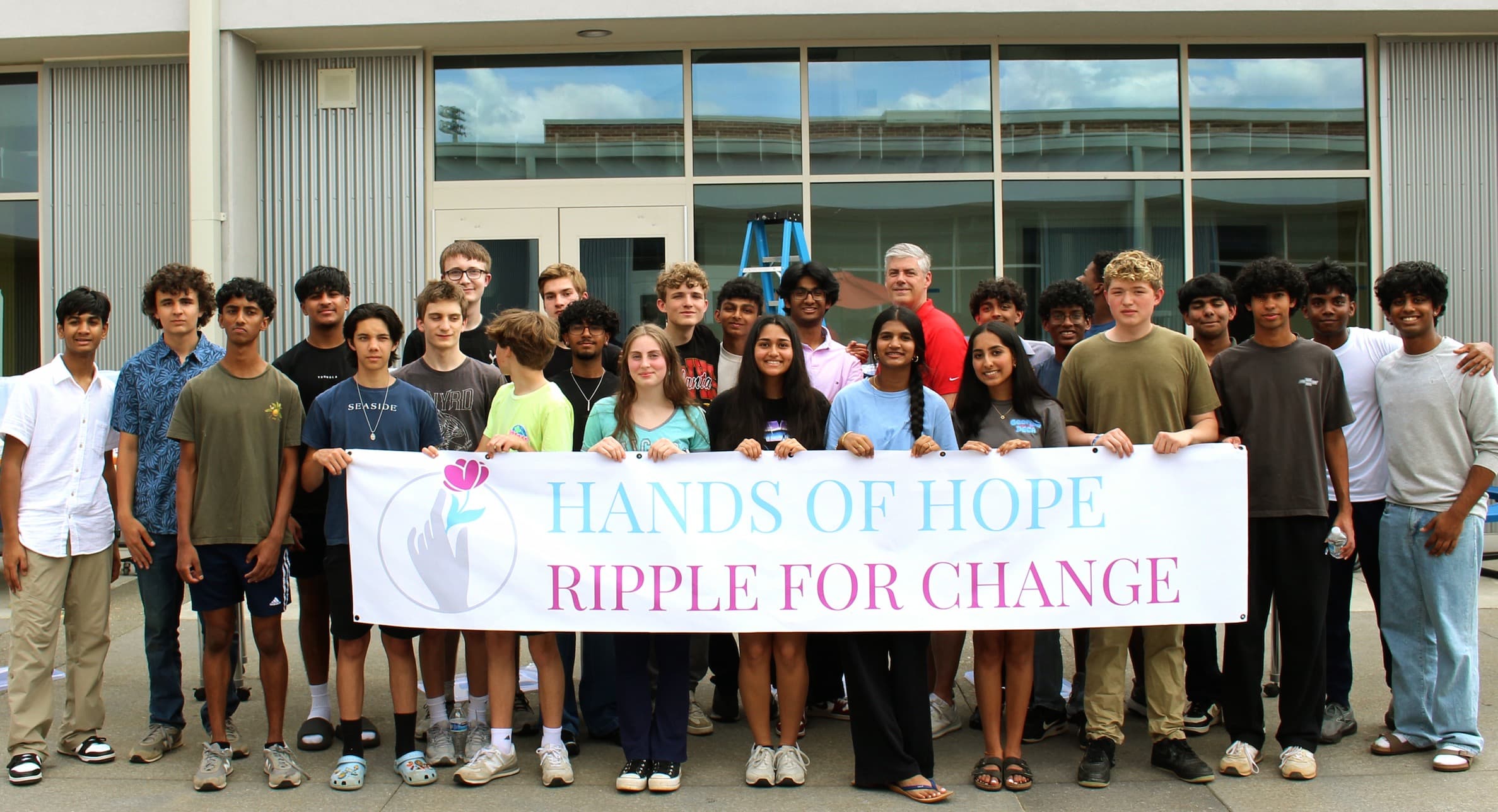 Hands of Hope Outreach students gathered behind the Ripple for Change banner